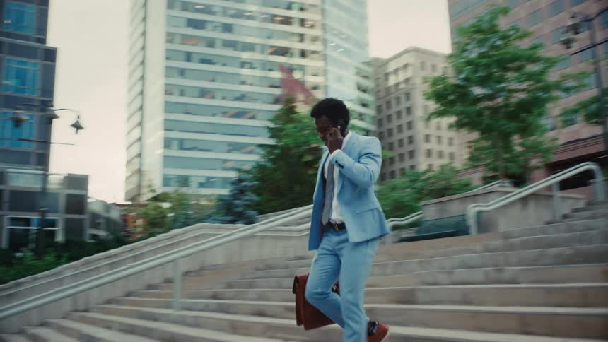 Man in a suit is having a phone call while running down the stairs outdoors in the city