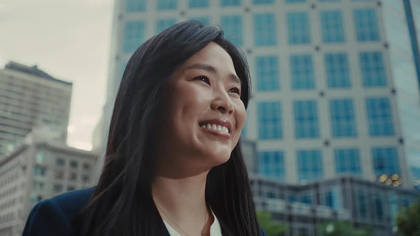 Woman stands near downtown buildings with a smile on her face as her hair moves in the breeze