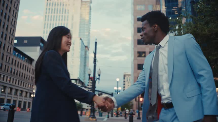 Man and woman meet on a downtown street shaking hands as they smile and talk