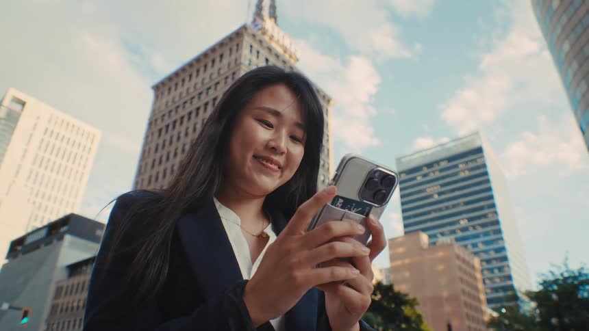 Woman smiles as she stands near downtown buildings texting on her phone