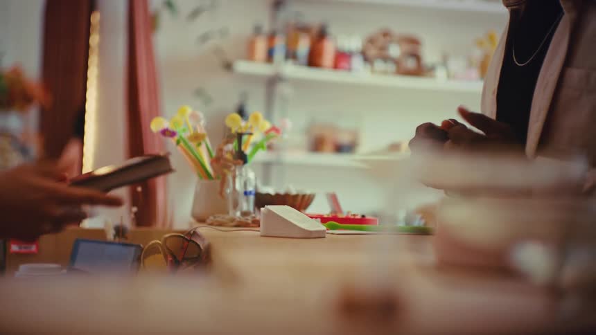 A person hands a black book titled spores to a worker at a shop counter during a transaction