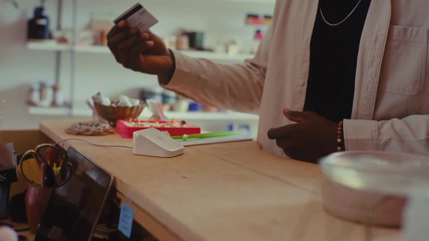 A black male customer inside a store swiping his credit card on the payment machine at the counter completing his purchase