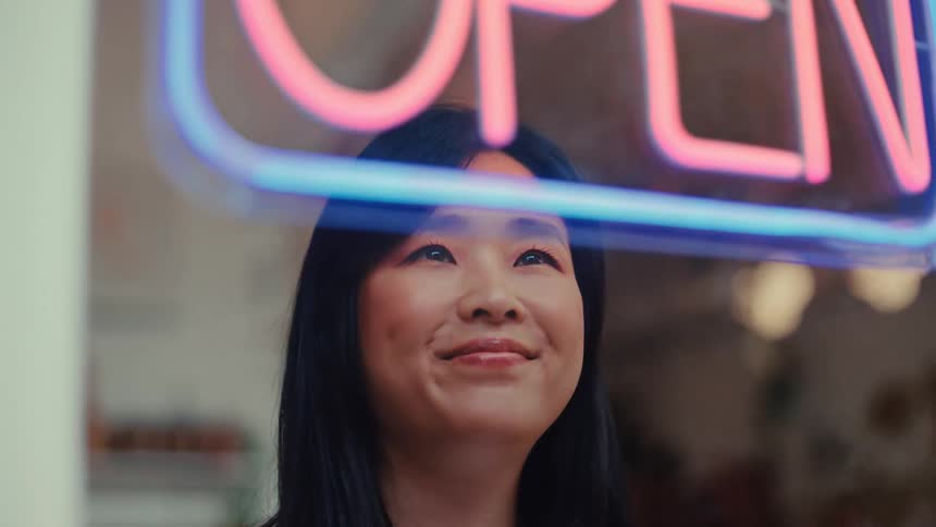 Smiling woman turning on a stores open neon light sign