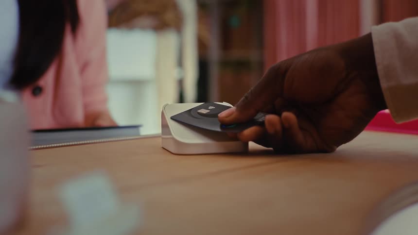 A hand taps a credit card on a payment terminal