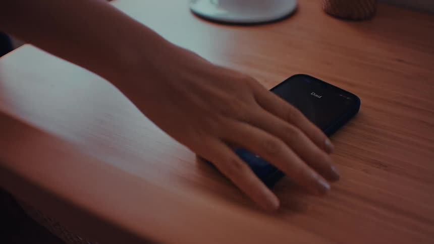 Closeup of a hand picking up a smartphone from a wooden desk