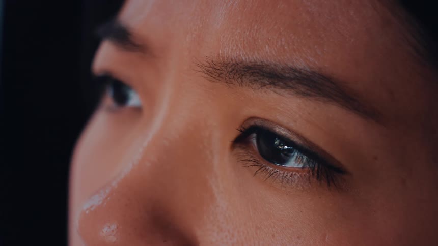 A young woman inside a room staring intently at a computer screen the glow of the display reflected clearly in her eye as she focuses on whats in front of her
