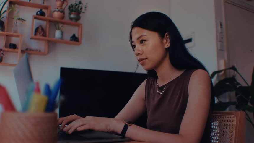 A woman works on a laptop at a home desk in a modern indoor workspace