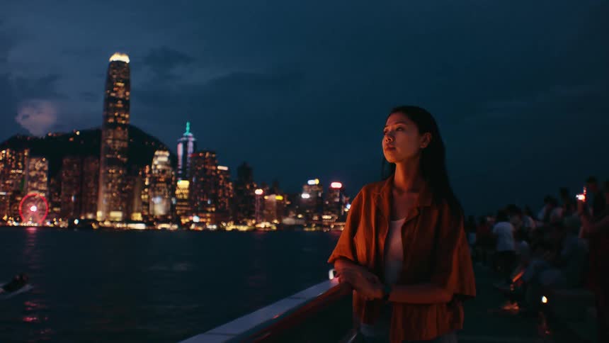 Woman gazes across the waterfront at the glowing city skyline at night
