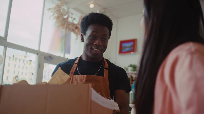 Store employee hands a box to a customer inside a welllit retail space