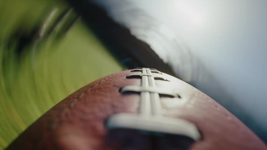 A pov shot football spirals rapidly through the air its white laces and textured leather distinct against a dizzying backdrop of blurred green grass and bright sky