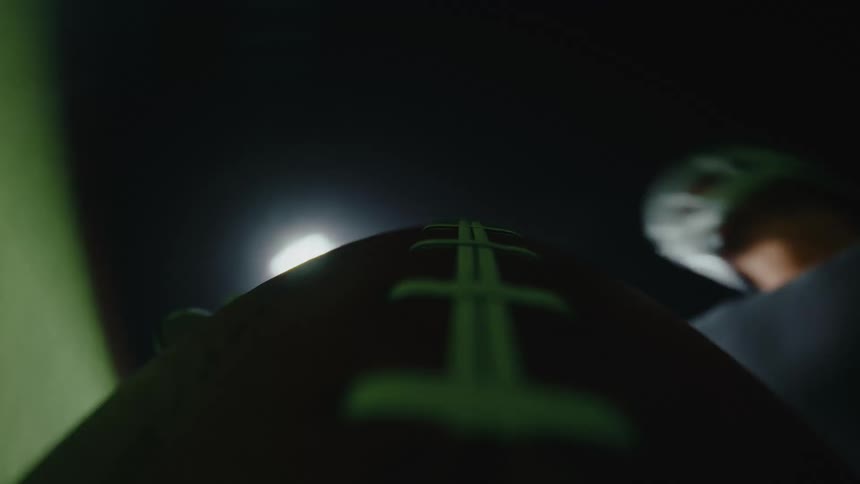 Football flying on the air next to a football player on a field outdoors during night time