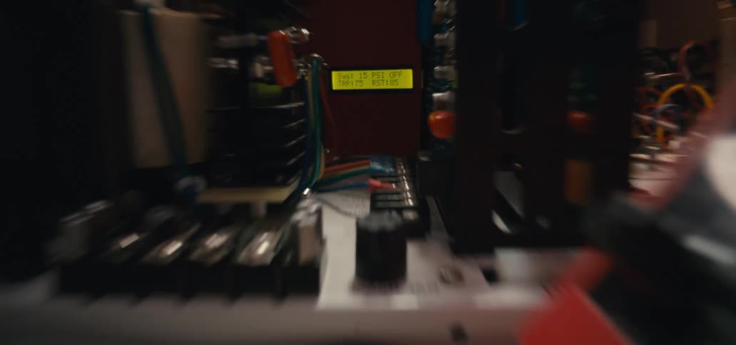 The video shows a closeup of an electronics workspace where a person is using a soldering iron on a green circuit board nearby equipment includes a digital display showing system pressure and a keyboard resting on the workbench