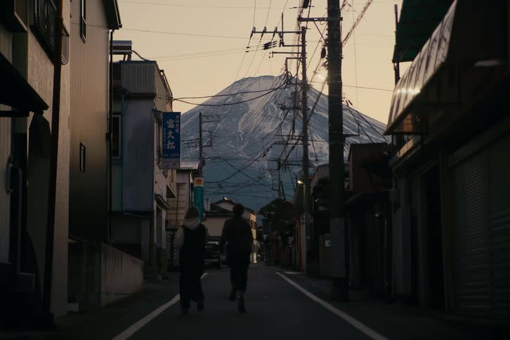 Two boys running and hugging on an alley of an urban area next to a mountain outdoors during dusk or dawn