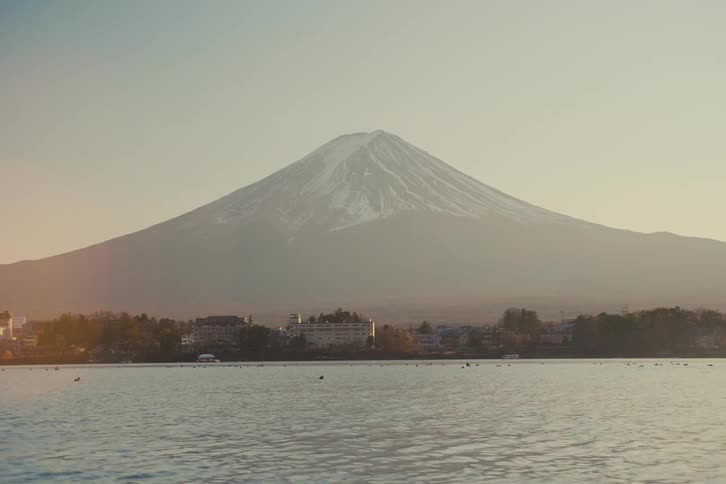 A snow capped mountain rises above a lakeside town under soft daylight