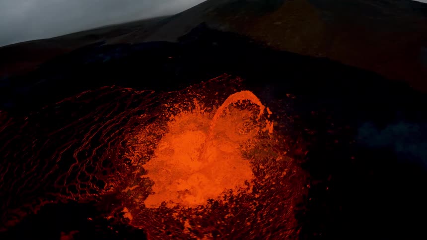 Glowing lava flow spreads across a dark volcanic surface during eruptive activity