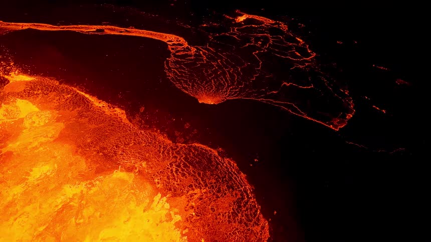 A seething expanse of molten lava churns and surges in vivid shades of yellow and orange its blistering surface edged by darker cooling crusts and glowing fissures