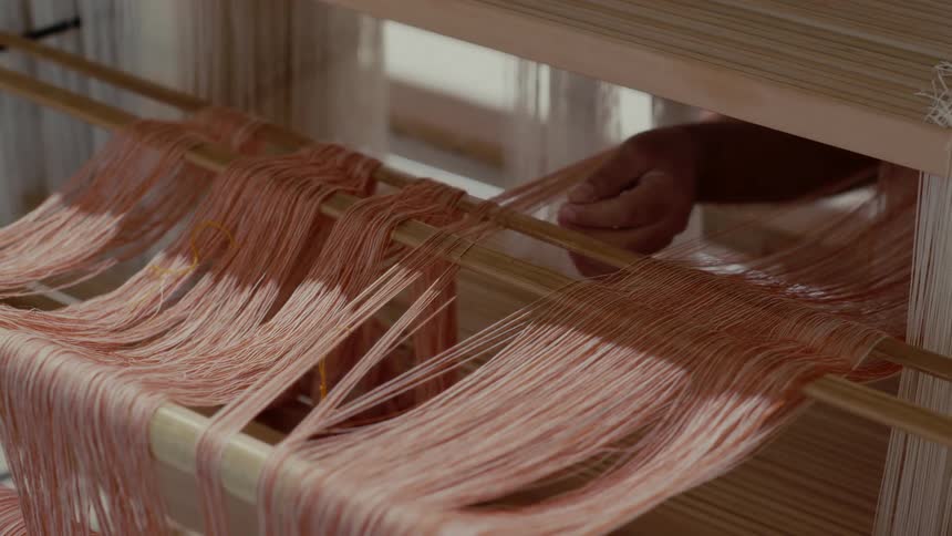 Pink threads are manually arranged on a wooden loom during a textile crafting process