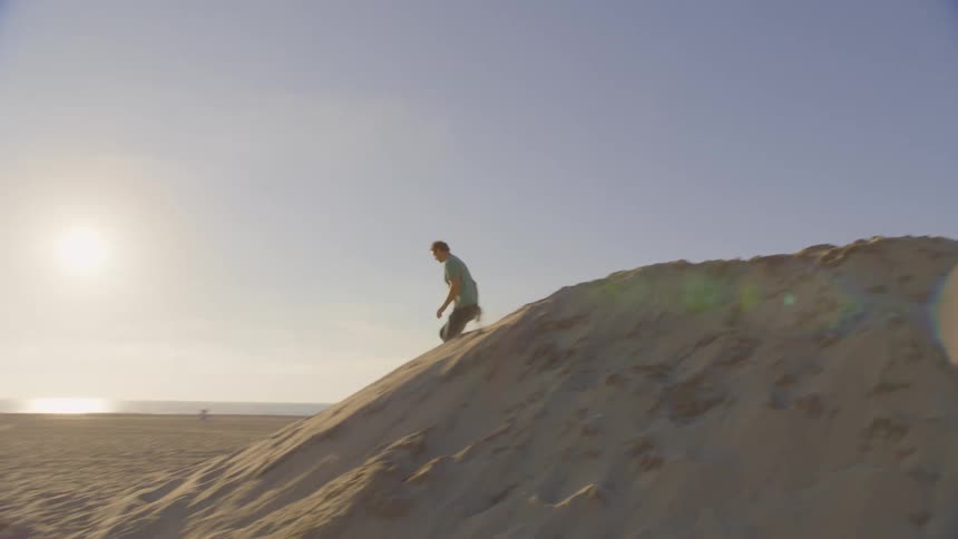 The man runs down the dune on the beach with his dog