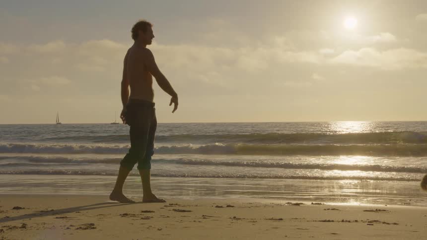 Man on the beach throwing a small ball for his golden retriever to fetch