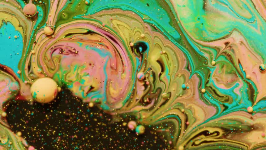 Vibrant swirls of green yellow and pink liquid paint blend together in a cosmic dance as small bubbles drift through the colorful currents
