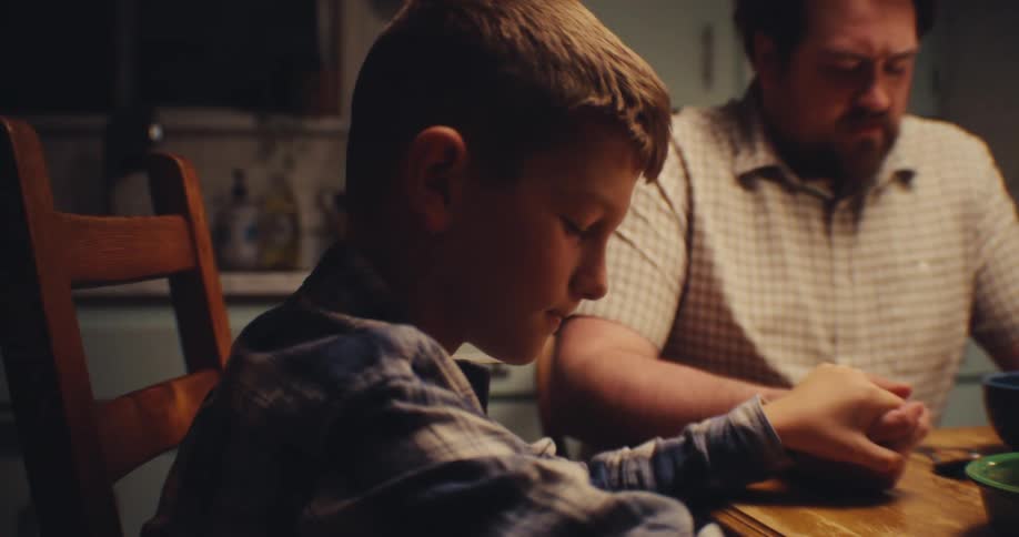 Boy sitting at a table holding hands with an adult and praying