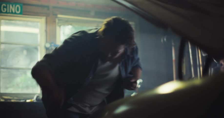 A man works on a car engine under an open hood in a garage