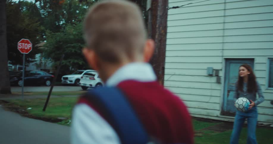A young schoolboy walks down a residential street past other children playing catch