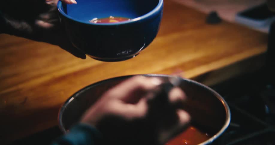 A child a woman and a man take turns ladling soup from a pot into green and blue bowls