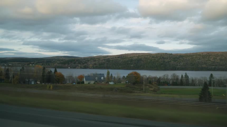 Moving view along a highway with a landscape of a lake and wooded mountains in the background