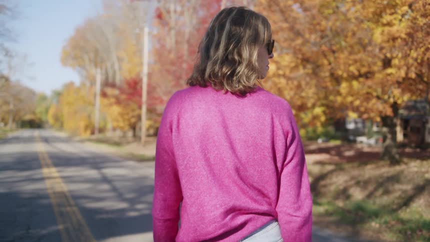 Woman walks down the middle of a neighborhood street with trees in bright fall colors