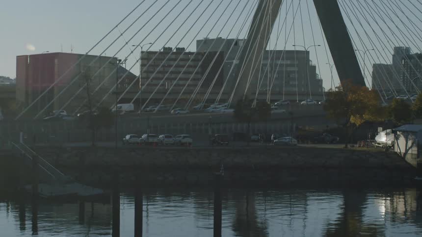 Cablestayed bridge spans an urban river with vehicle traffic and residential buildings in the background