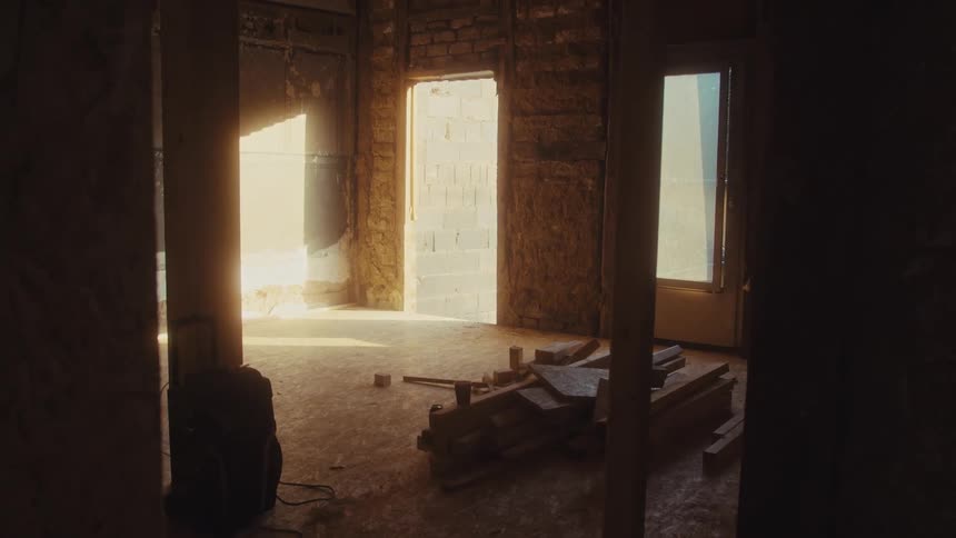 Warm sunlight streams into a dusty unfinished room under renovation highlighting exposed brick walls and a pile of lumber on the floor