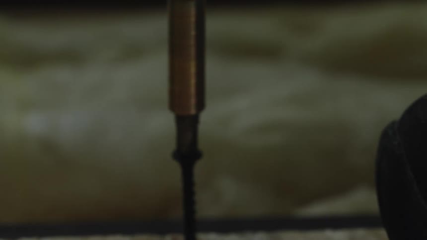 An electric screwdriver drives a screw into a piece of wooden board