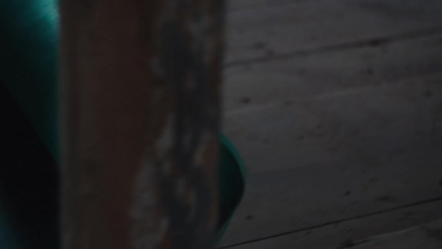 A persons hands are shown unrolling a textured teal yoga mat across a rustic wooden floorthe camera pans to the right following the length of the mat as it settles into a dark moody interior space