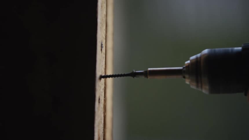 Power drill drives a screw into a wooden panel during assembly work