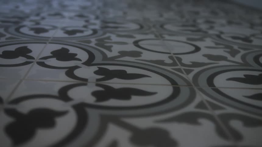 The video shows a closeup lowangle shot of a tiled floor featuring a repeating geometric and floral pattern in shades of gray black and white the camera slowly glides forward across the surface keeping the focus sharp on the tiles in the foreground