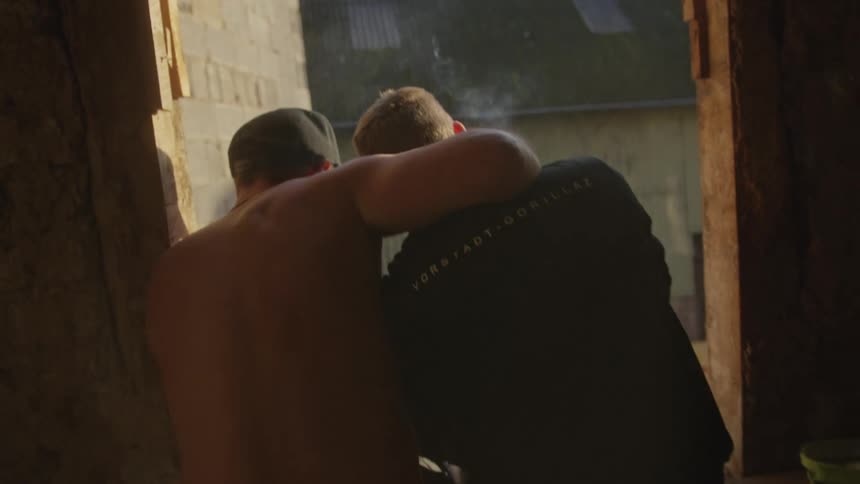Two young adult men sitting on a window hugging indoors during day time