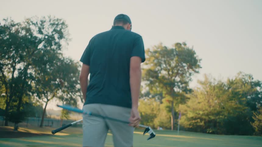 Man picking up a golf club and walking across the course