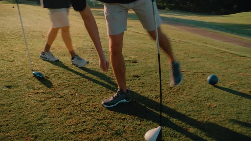 Two people putting down golf balls on a tee box