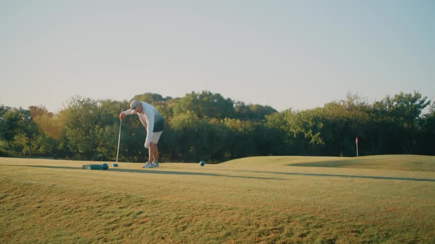 Golfer positions the ball on the tee on an open course surrounded by vegetation