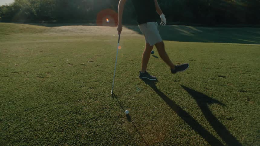 Man walks across the golf course carrying his golf club and kicks the grass near the balls
