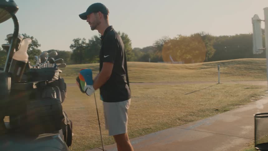 Golfer organizes equipment beside the golf cart on the course