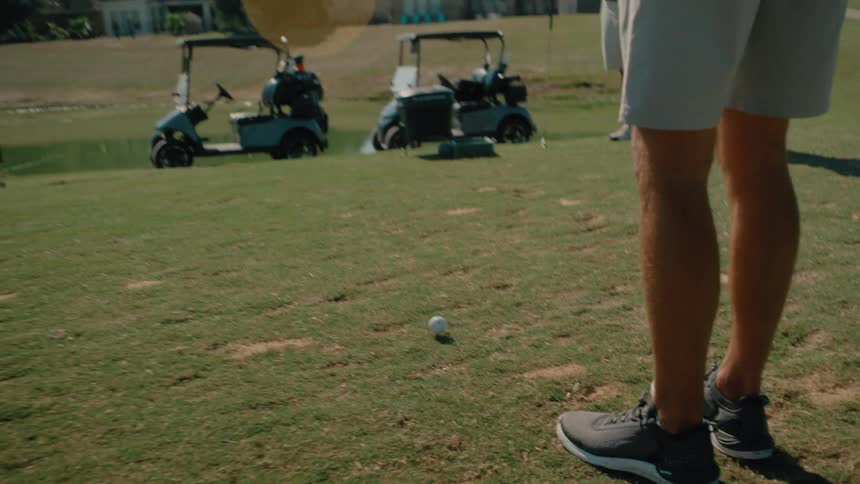Golfer prepares a short shot on the fairway with golf carts parked in the background