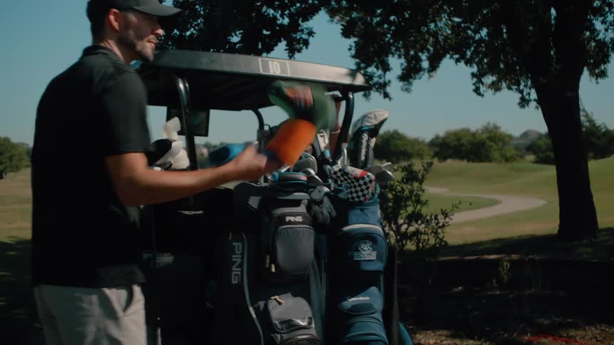 Man playing a hole on a golf course puts his club back in the bag on the back of a golf cart