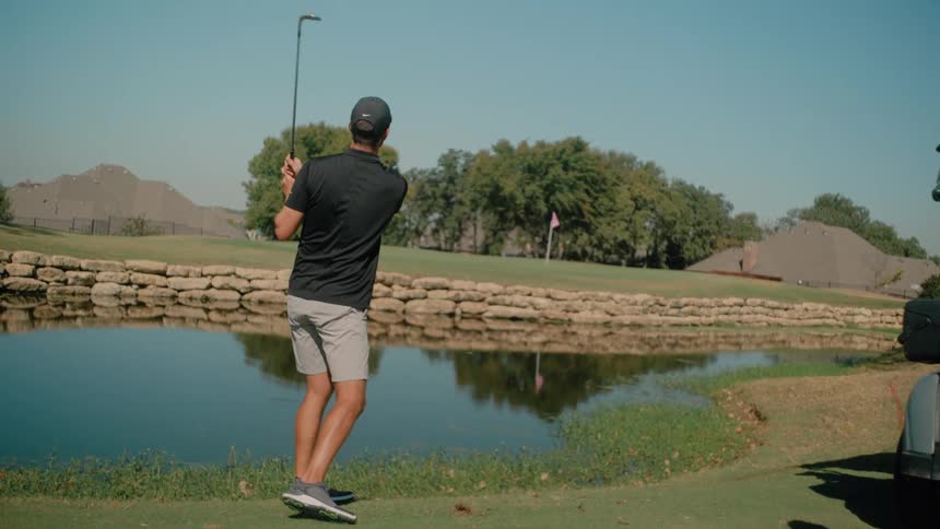 Man hits a golf shot at a target crossing a lake