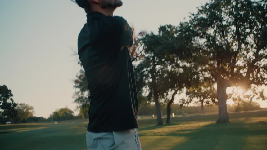 Golfer executes a shot and follows the clubs motion under evening light