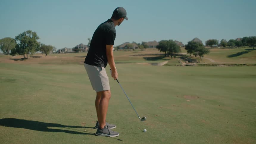 Man carries his golf club as he steps up to the ball and practices his swing and then swings and hits the ball