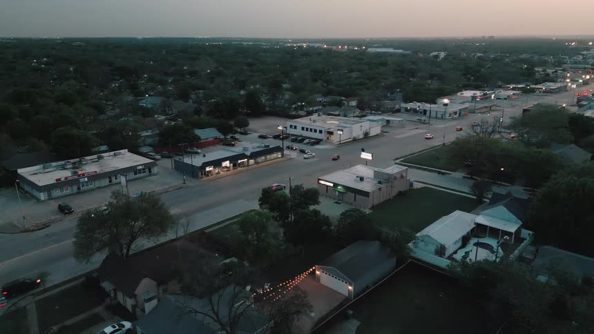 Aerial view of an urban block at dusk with commercial buildings road intersection and light traffic