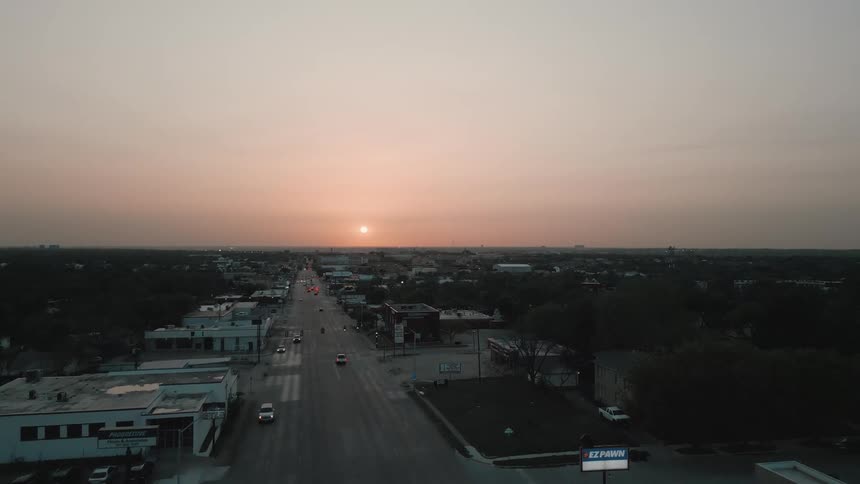 Aerial view of an urban avenue at dusk with light traffic and a sunsetlit horizon