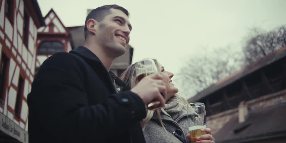Couple holds beer glasses while observing the outdoor urban setting